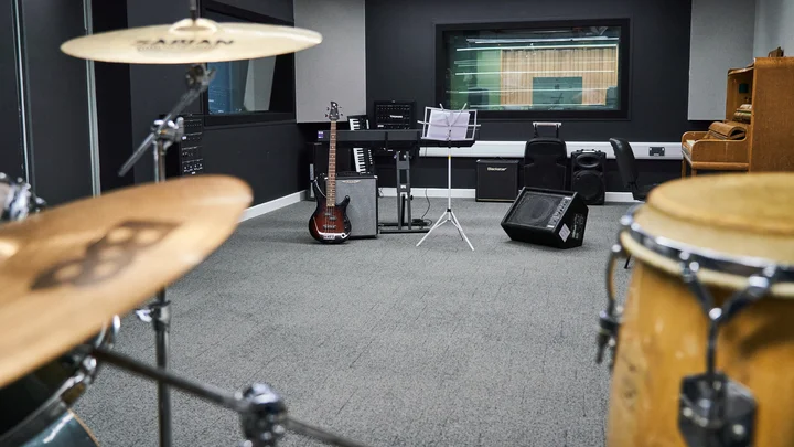 A band rehearsal room with drums, an electric guitar, speakers, keyboards and a piano
