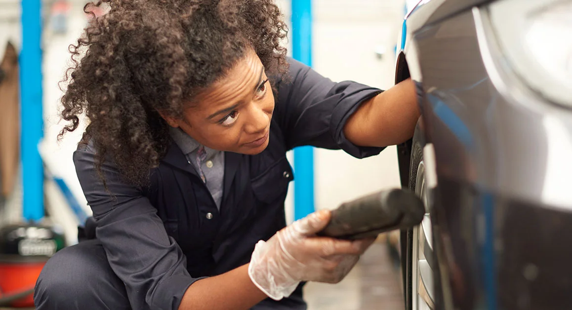 College learner inspecting and working on a car wheel in an auto repair shop.