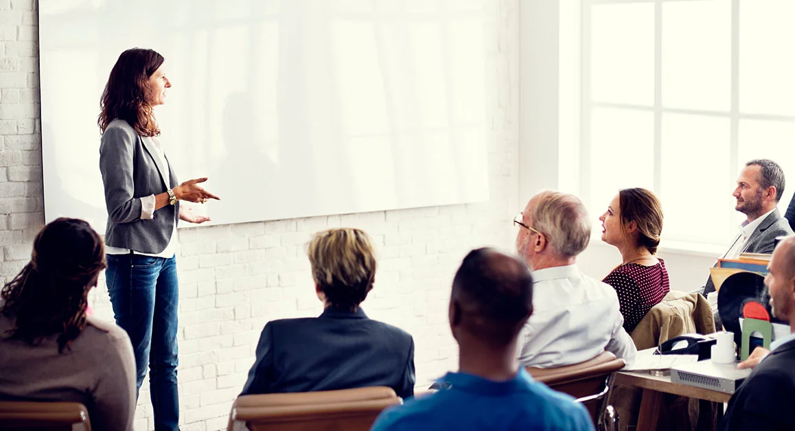 Person presenting to a group of attendees in a classroom or workshop setting.