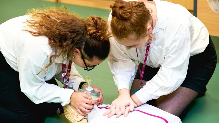 Learners practising CPR during aviation safety training, performing chest compressions and using a resuscitation mask on a training manikin.