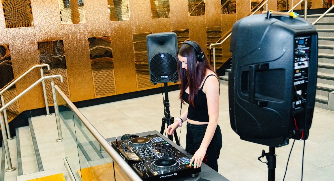 A learner DJing on professional decks with speakers set up in a modern indoor college area.