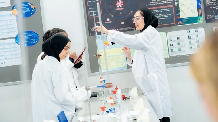 Science learners working together in a laboratory, carrying out a chemistry experiment with lab coats, glassware, and equipment.